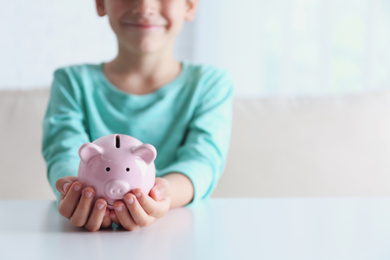 Photo of Little boy with piggy bank at white table indoors, closeup. Space for text