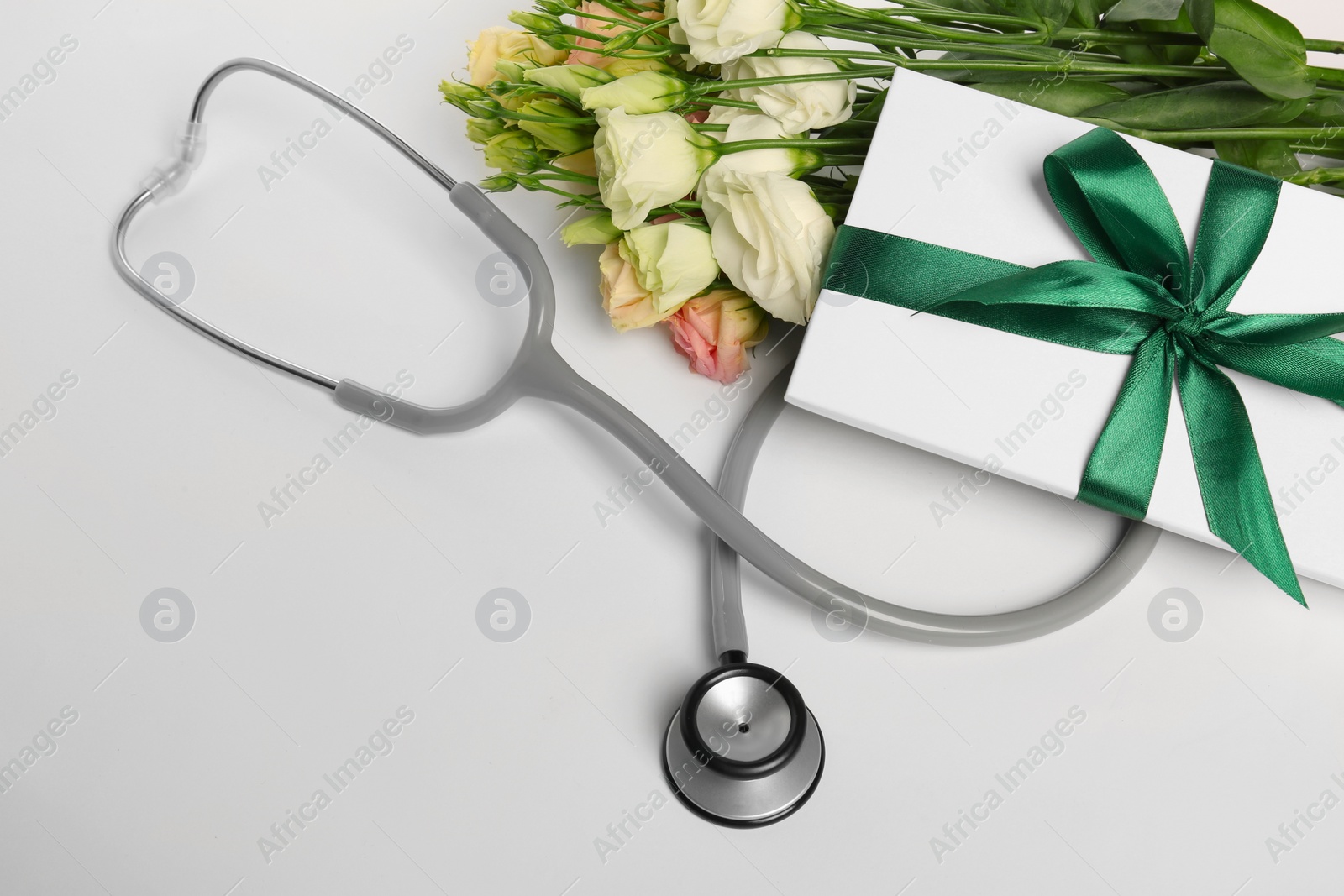 Photo of Stethoscope, gift box and eustoma flowers on white background. Happy Doctor's Day