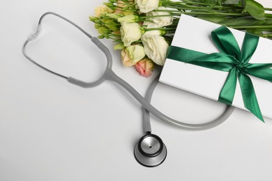 Stethoscope, gift box and eustoma flowers on white background. Happy Doctor's Day
