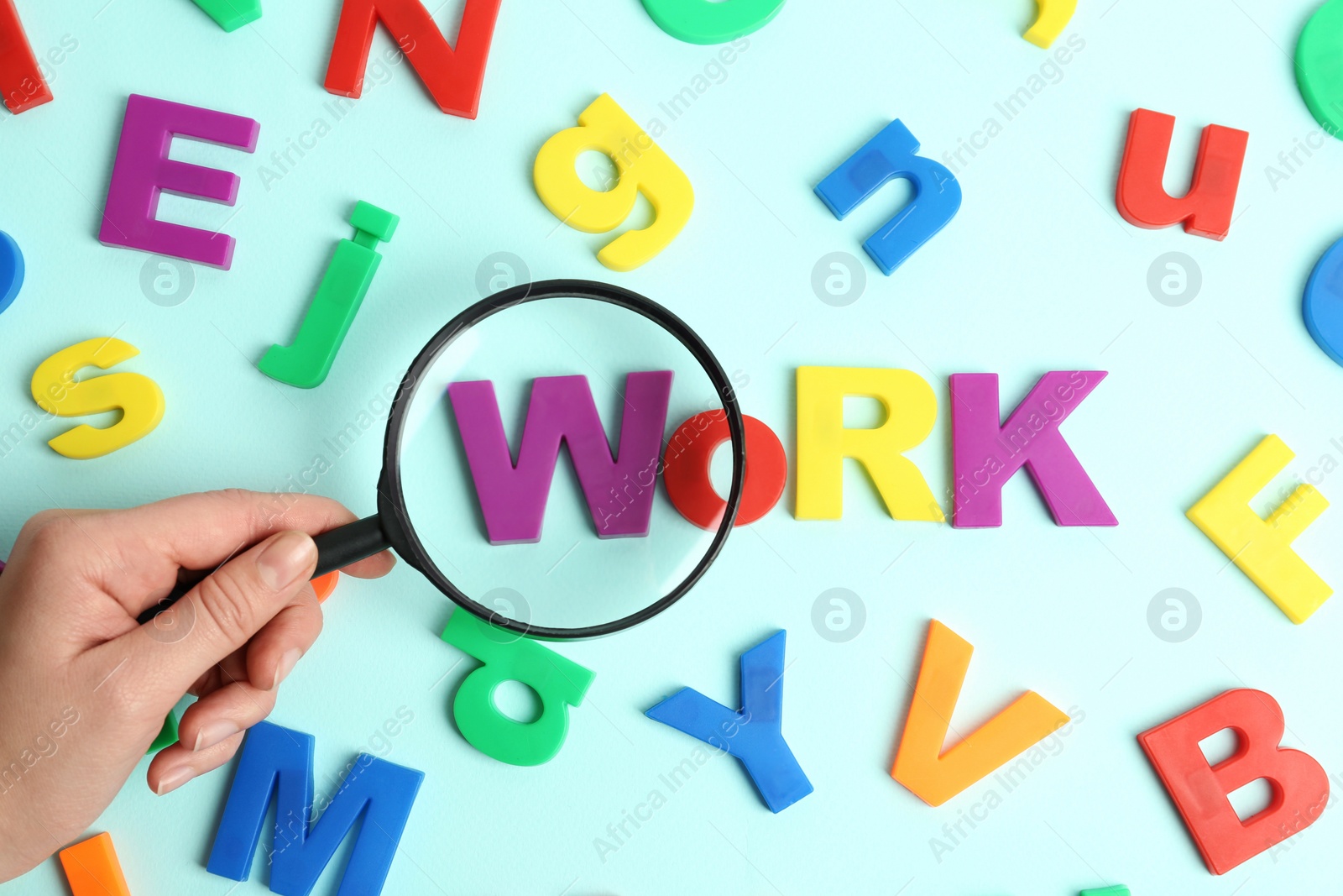 Photo of Woman holding magnifying glass over word WORK made with magnet letters on light blue background, top view. Search concept