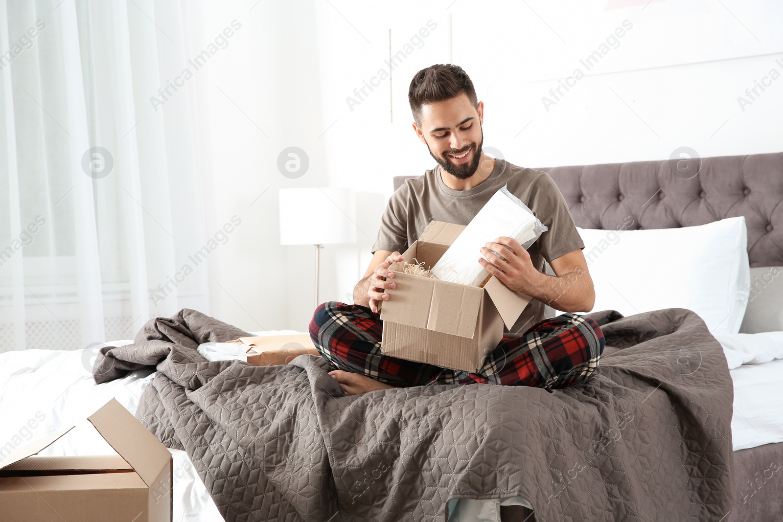 Photo of Young man opening parcel in bedroom at home