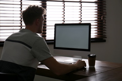 Lonely man sitting at computer with empty screen indoors