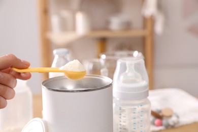 Photo of Woman preparing infant formula at table indoors, closeup. Baby milk