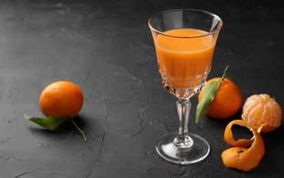 Photo of Tasty tangerine liqueur in glass and fresh fruits on black textured table. Space for text