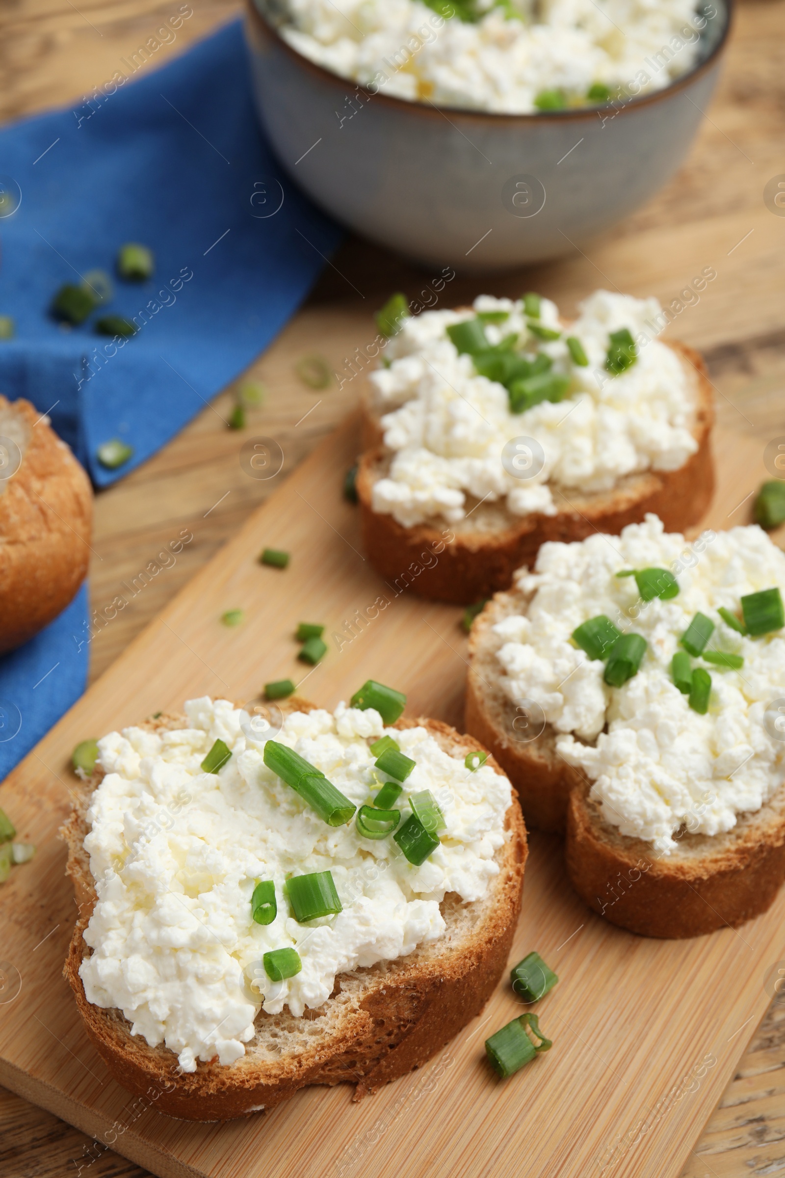 Photo of Bread with cottage cheese and green onion on wooden board, closeup