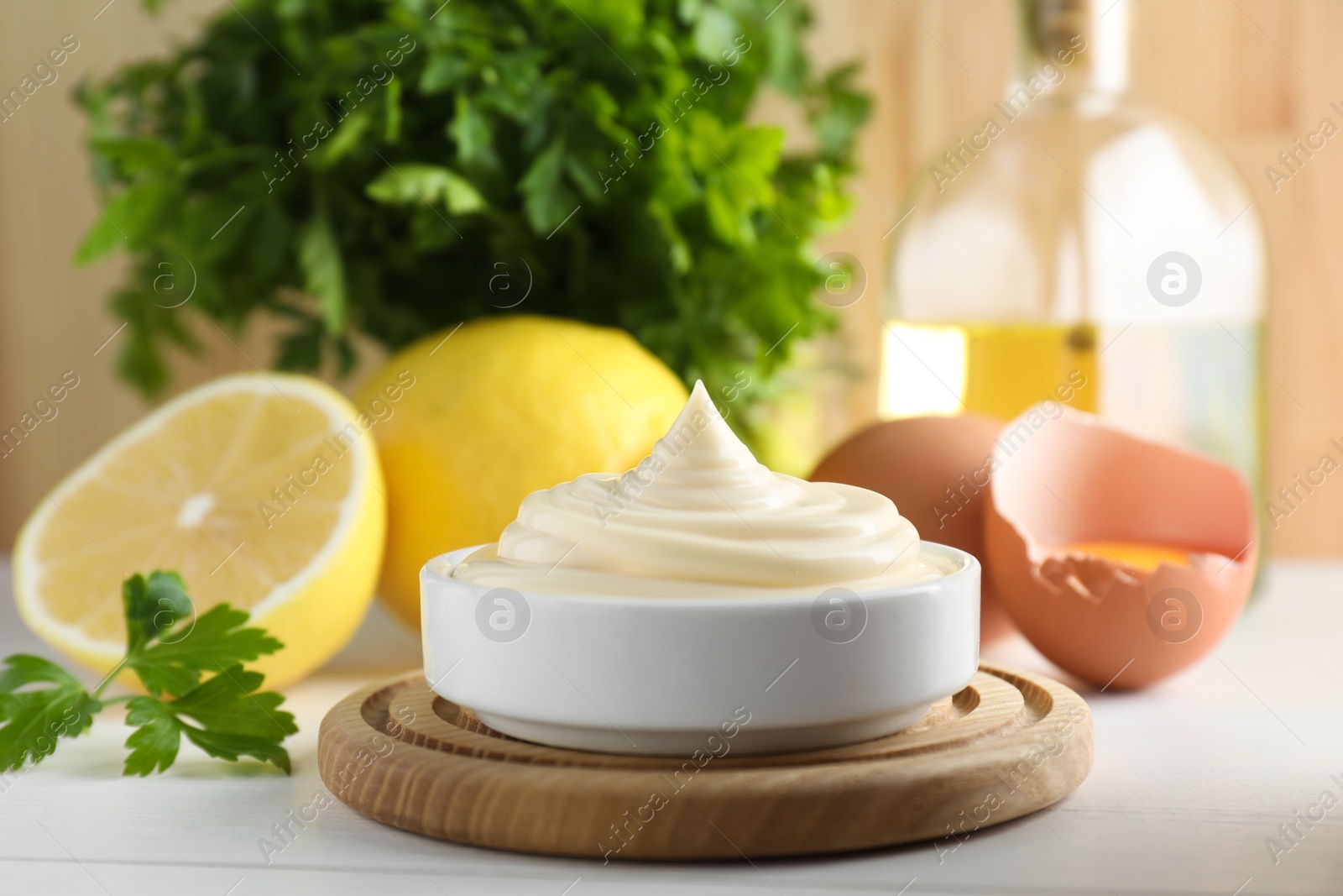 Photo of Fresh mayonnaise sauce in bowl and ingredients on white wooden table, closeup