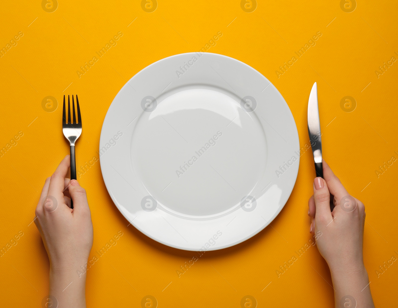 Photo of Woman with empty plate and cutlery on orange background, top view