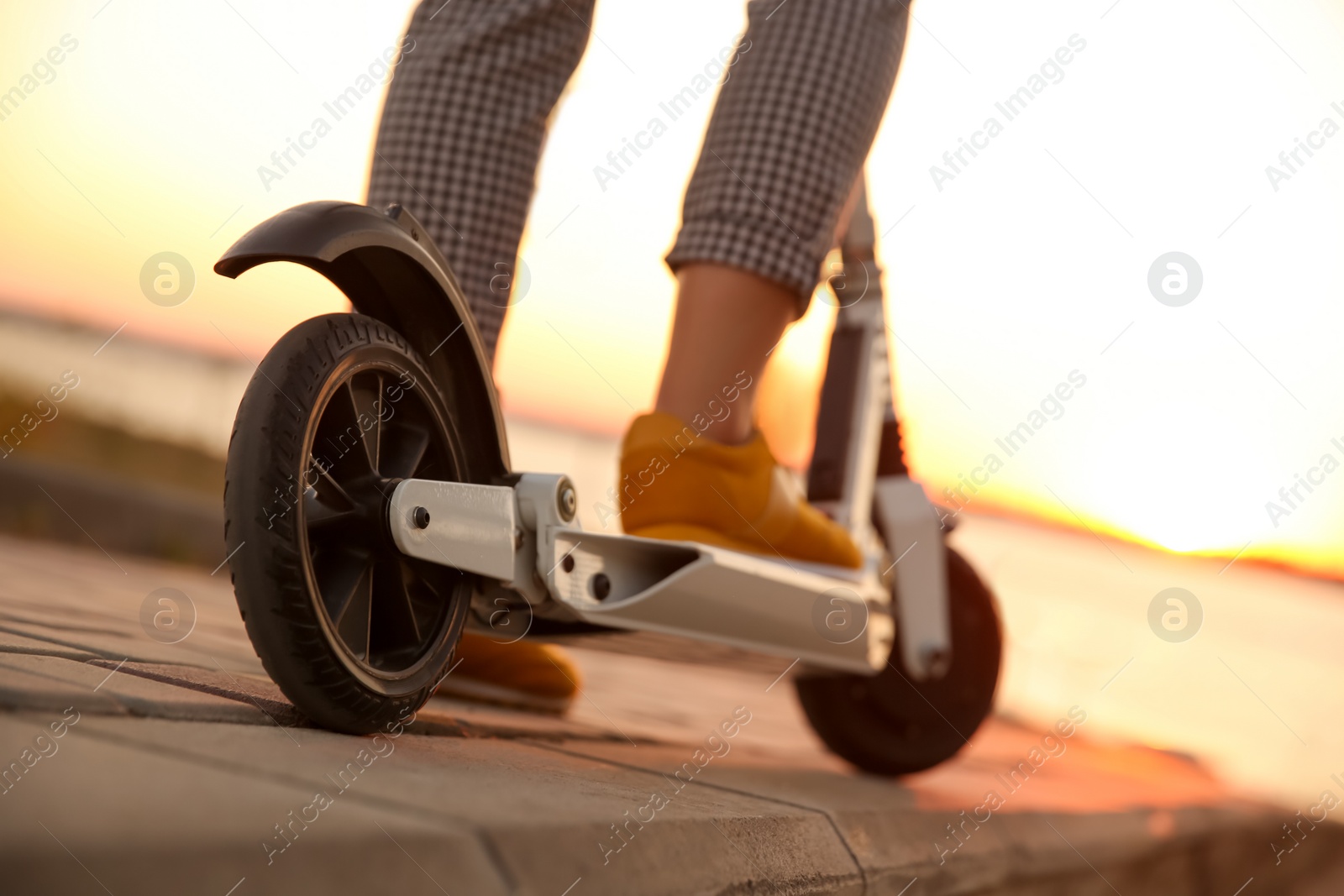 Photo of Woman riding electric kick scooter outdoors at sunset, closeup