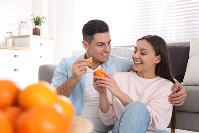 Photo of Happy couple with tangerines near sofa at home