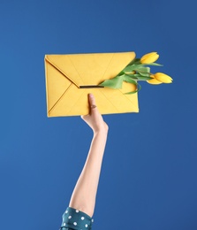 Photo of Woman holding elegant clutch with spring flowers on blue background, closeup