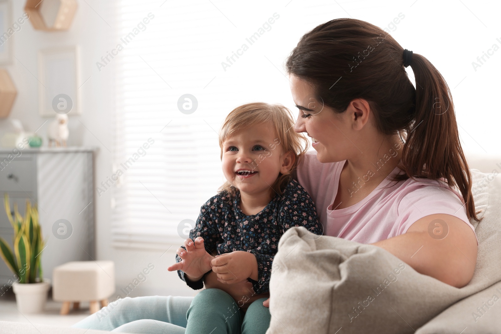 Photo of Mother with her cute little daughter on sofa at home, space for text