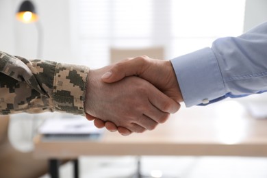Photo of Soldier and businessman shaking hands indoors, closeup