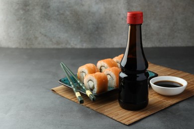 Tasty soy sauce, chopsticks and sushi rolls with salmon on grey table. Space for text