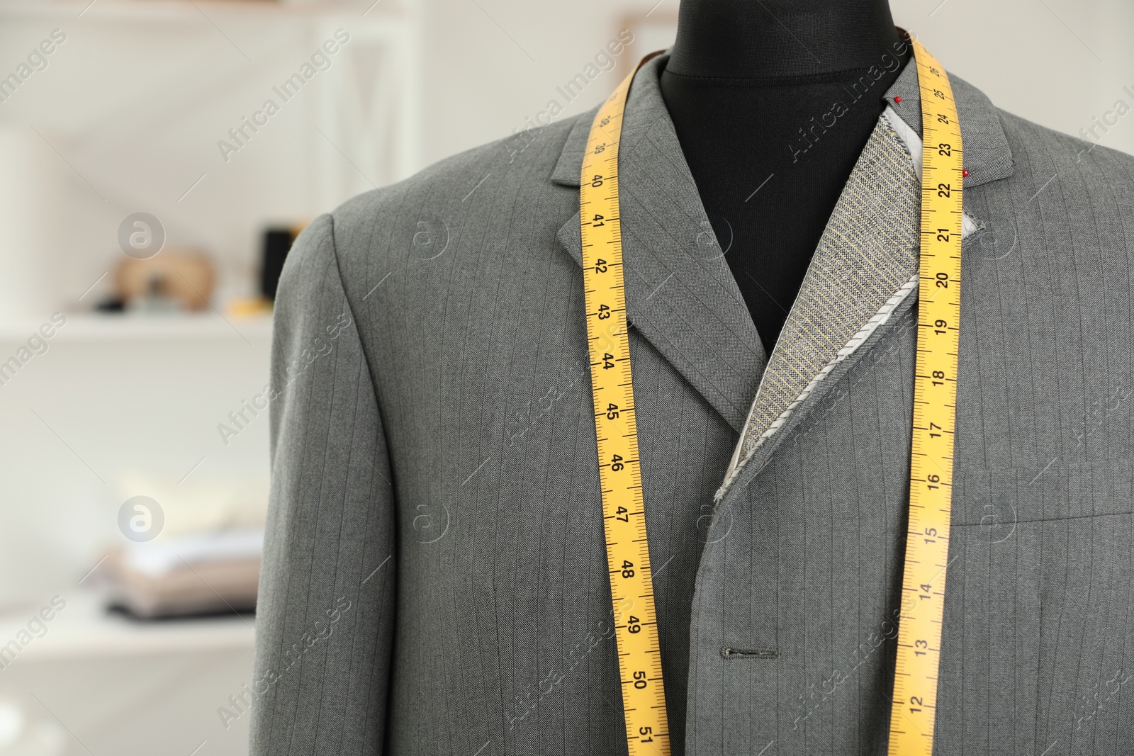 Photo of Mannequin with unfinished jacket and measuring tape in tailor shop, closeup