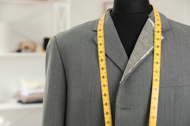 Photo of Mannequin with unfinished jacket and measuring tape in tailor shop, closeup
