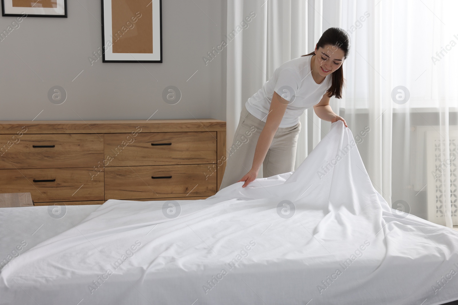 Photo of Young woman changing bed linens at home