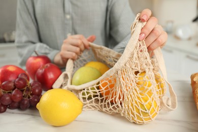 Photo of Woman with string bag of fresh fruits at light marble table, closeup