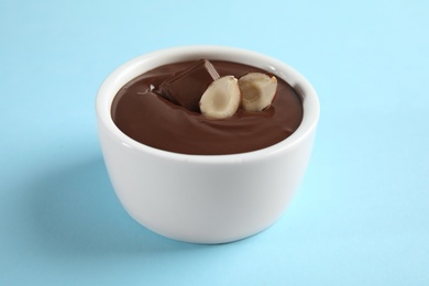 Photo of Ceramic bowl with sweet chocolate cream and hazelnuts on color background