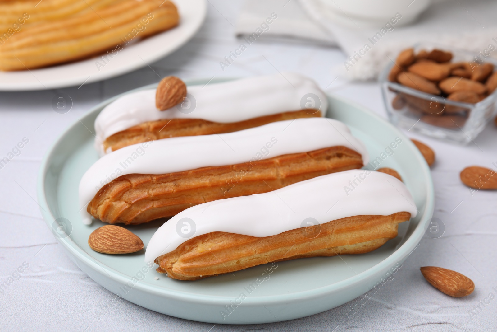 Photo of Delicious eclairs covered with glaze and almonds on white textured table, closeup