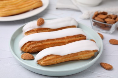 Delicious eclairs covered with glaze and almonds on white textured table, closeup