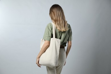 Woman with blank eco friendly bag on light background, back view