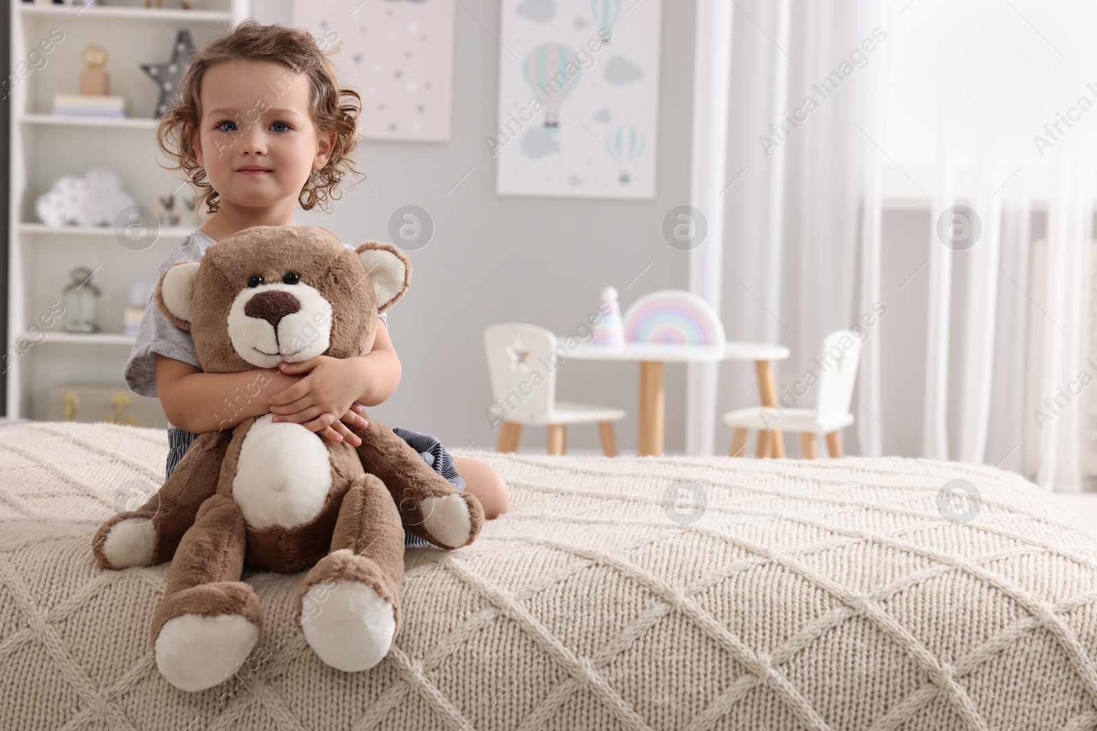 Photo of Cute little girl with teddy bear on bed at home