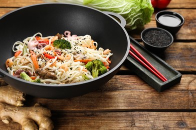 Stir fried noodles with seafood and vegetables in wok on wooden table