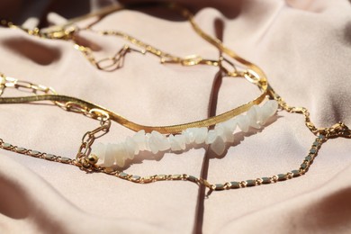 Photo of Metal chains with gemstones on pale pink fabric, closeup. Luxury jewelry