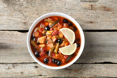 Photo of Meat solyanka soup with sausages, olives and vegetables in bowl on wooden table, top view