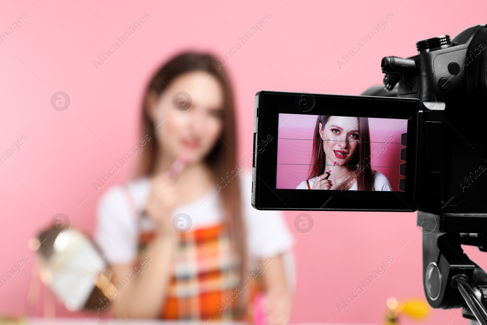 Photo of Beauty blogger filming make up tutorial on pink background, focus on camera