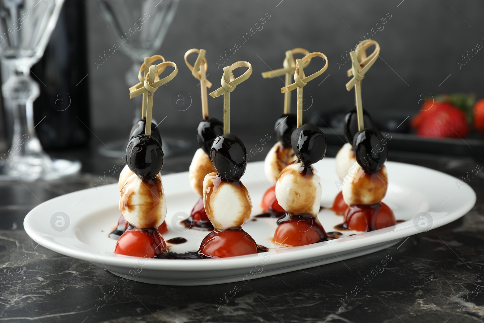 Photo of Tasty canapes with black olives, mozzarella and cherry tomatoes on dark textured table, closeup