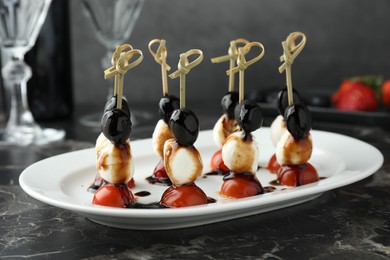 Photo of Tasty canapes with black olives, mozzarella and cherry tomatoes on dark textured table, closeup