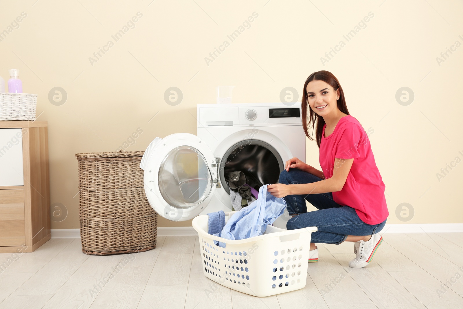 Photo of Young woman taking laundry out of washing machine at home