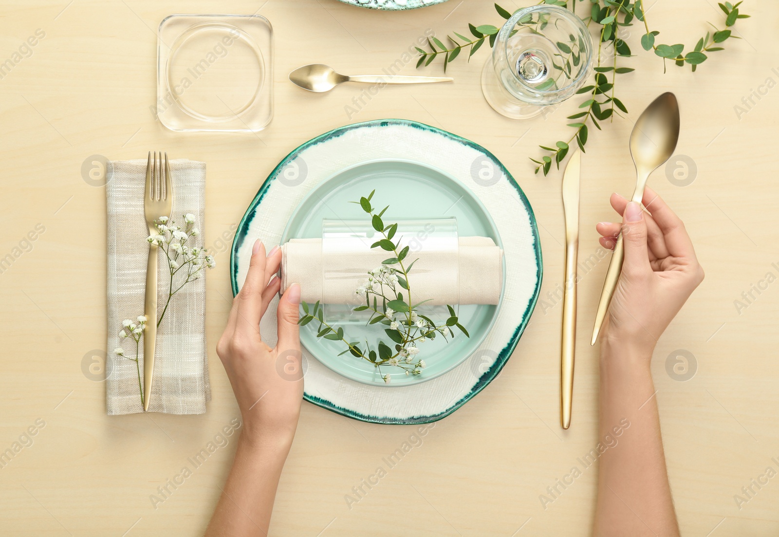 Photo of Woman setting table with green leaves for festive dinner, top view