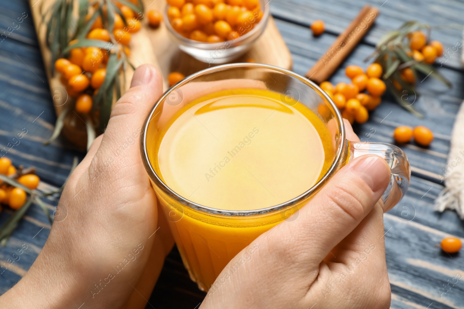 Photo of Woman with cup of fresh sea buckthorn tea at blue wooden table, closeup