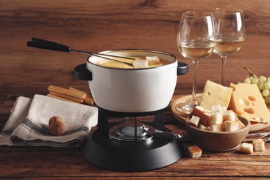 Photo of Pot of tasty cheese fondue, snacks and wine on wooden table