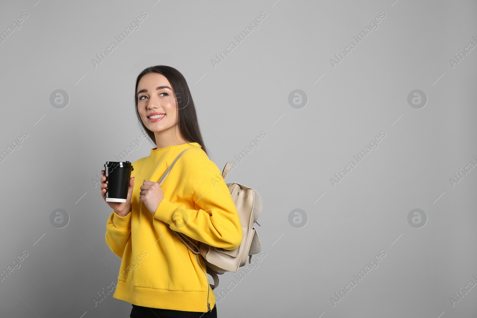 Photo of Beautiful young woman with stylish leather backpack and cup of coffee on grey background. Space for text