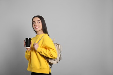 Beautiful young woman with stylish leather backpack and cup of coffee on grey background. Space for text