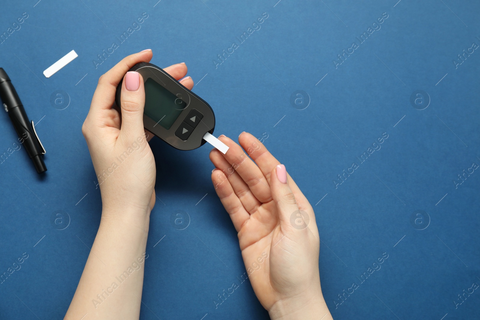 Photo of Diabetes. Woman checking blood sugar level with glucometer on blue background, top view. Space for text