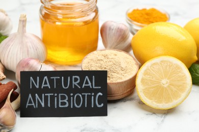 Photo of Different fresh products and card with phrase Natural Antibiotic on white marble table, closeup