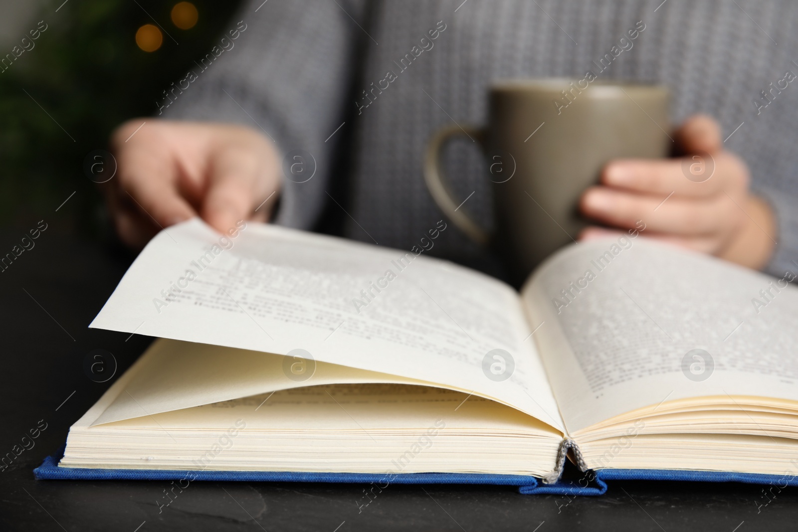 Photo of Woman with cup of beverage reading book at table, closeup