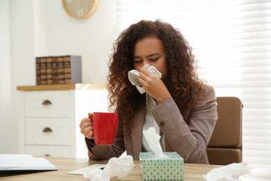 Photo of Sick African-American woman at workplace. Influenza virus
