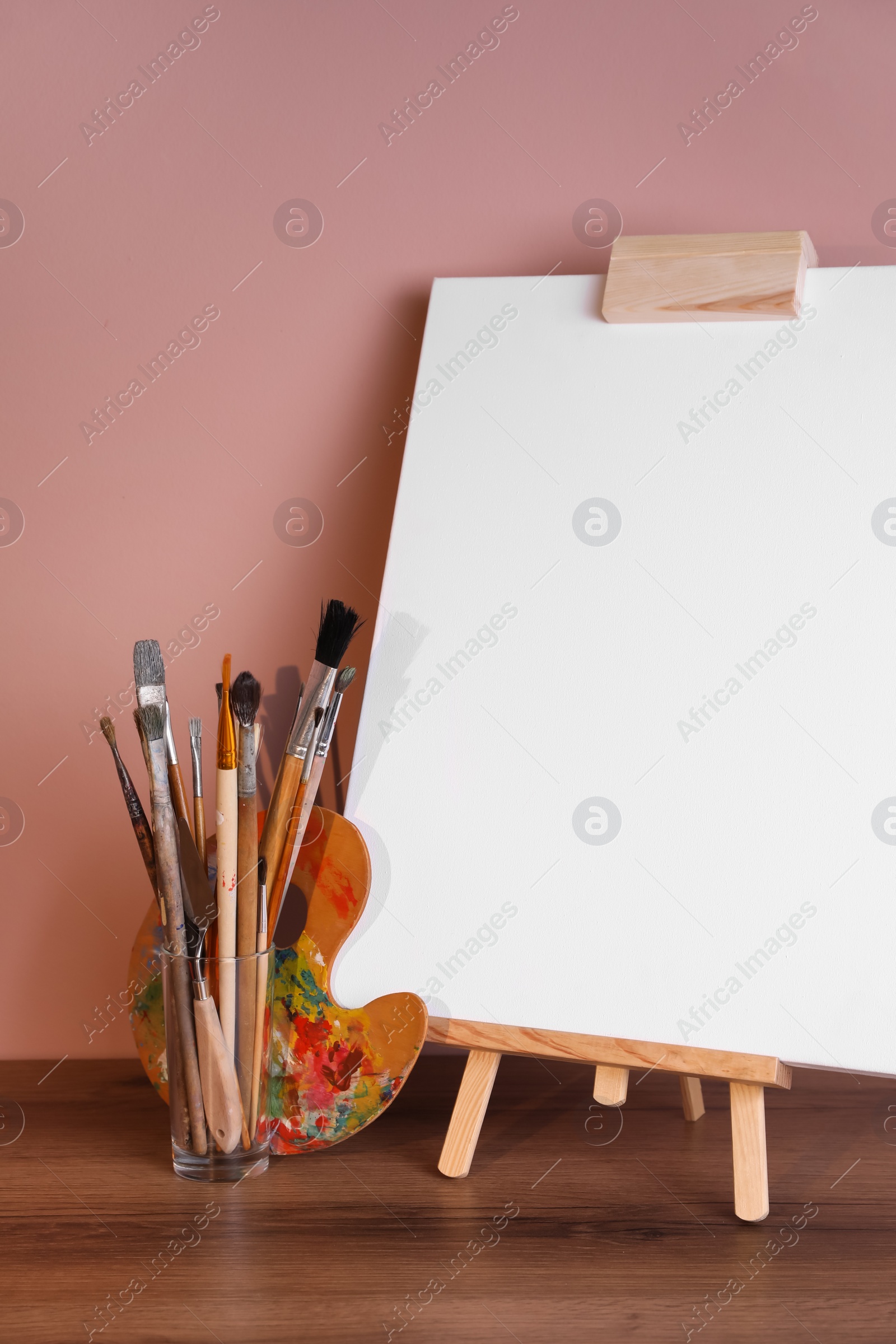 Photo of Easel with empty canvas and art supplies on wooden table