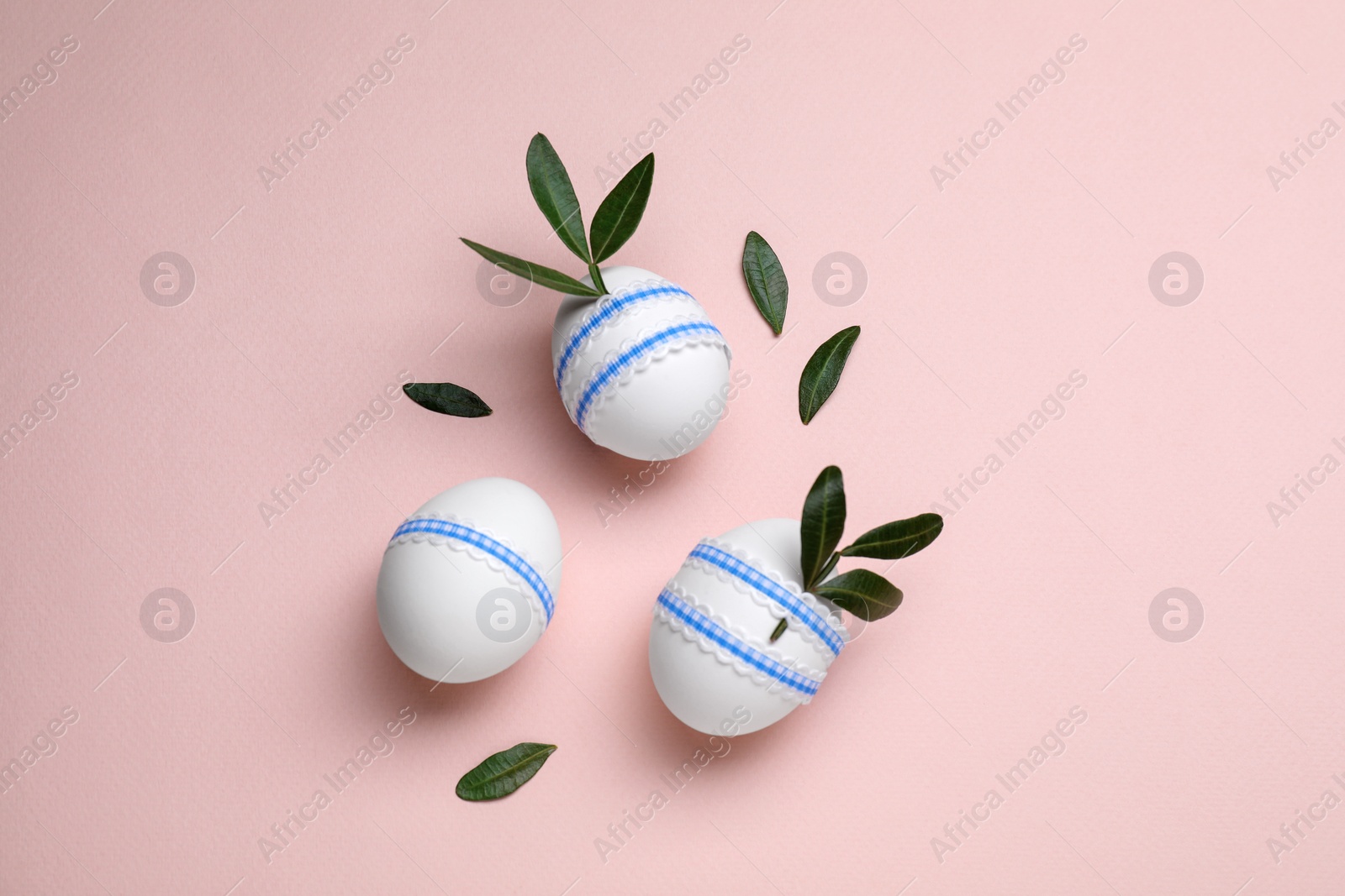 Photo of Beautifully decorated Easter eggs and green leaves on pale pink background, flat lay