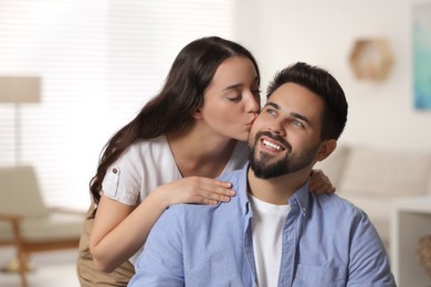 Cute couple. Woman kissing her smiling boyfriend at home