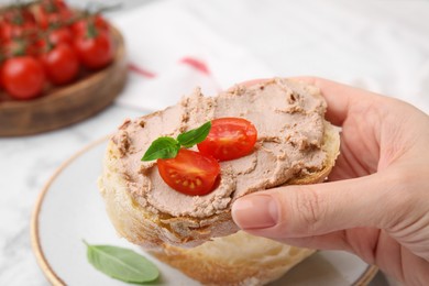 Photo of Woman holding delicious liverwurst sandwich with tomatoes and basil at table, closeup