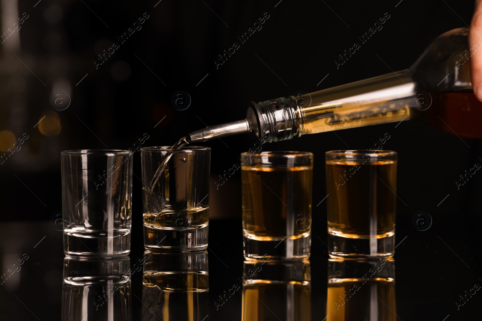 Photo of Pouring alcohol drink from bottle into shot glass at mirror counter, closeup