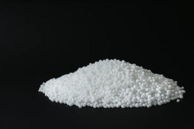 Photo of Pellets of ammonium nitrate on black background, space for text. Mineral fertilizer