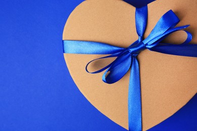 Photo of Beautiful heart shaped gift box with bow on blue background, top view