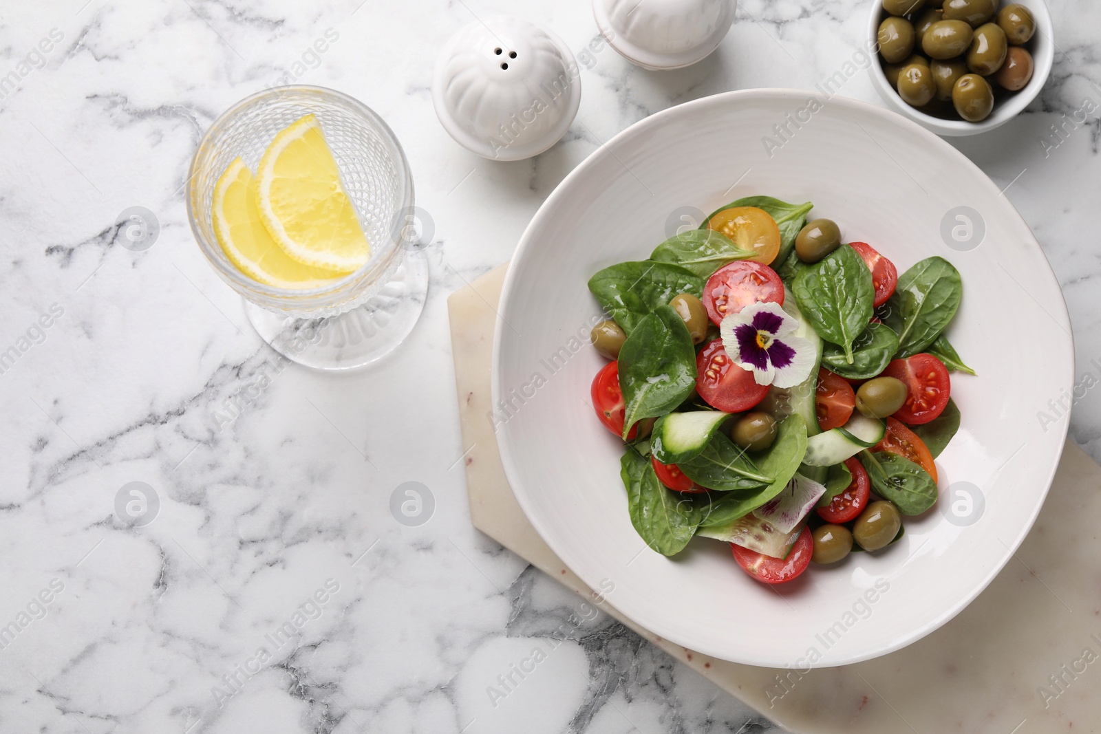 Photo of Delicious salad with vegetables and olives served on white marble table, flat lay